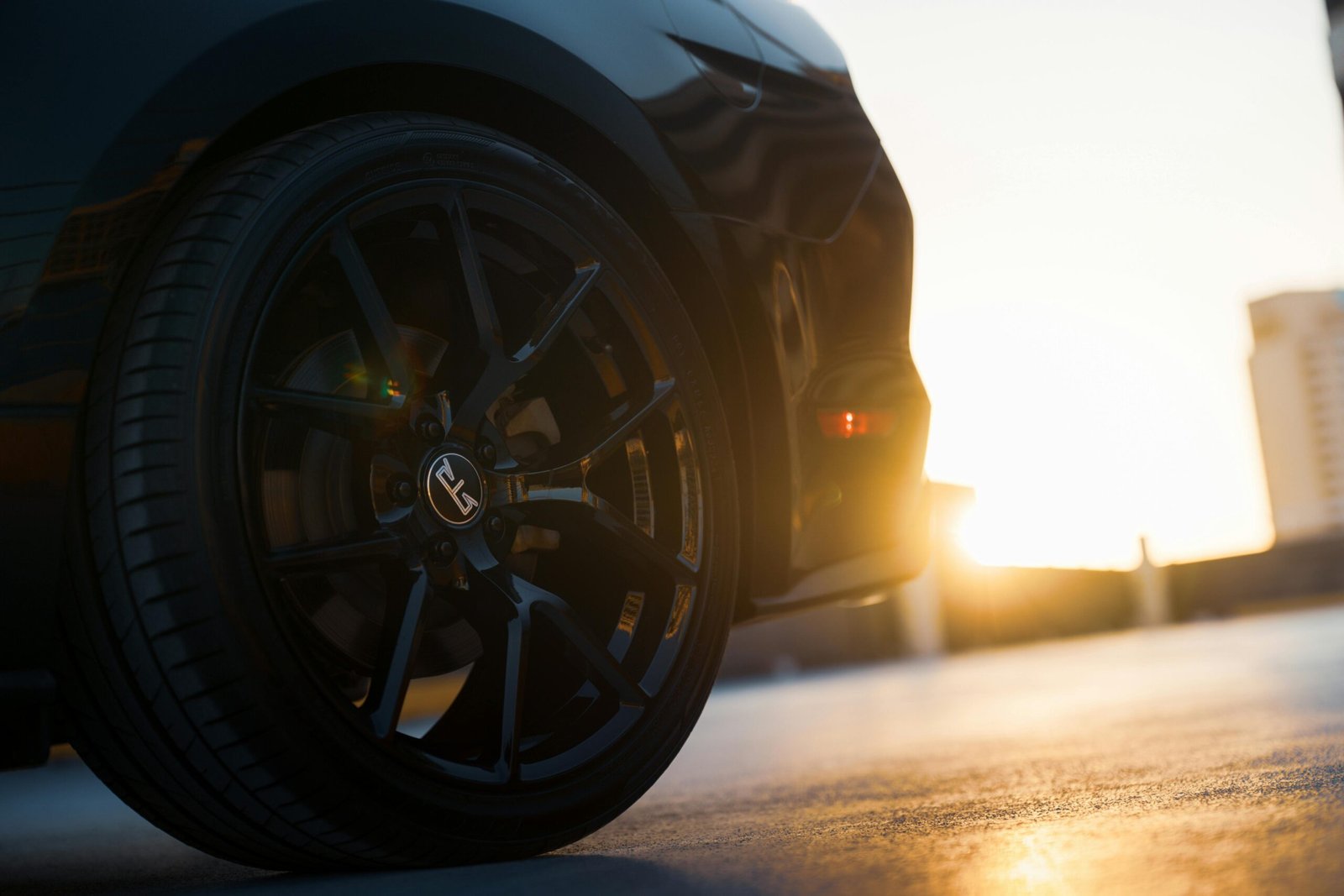 Detailed view of a sleek black car wheel and tire during sunset.