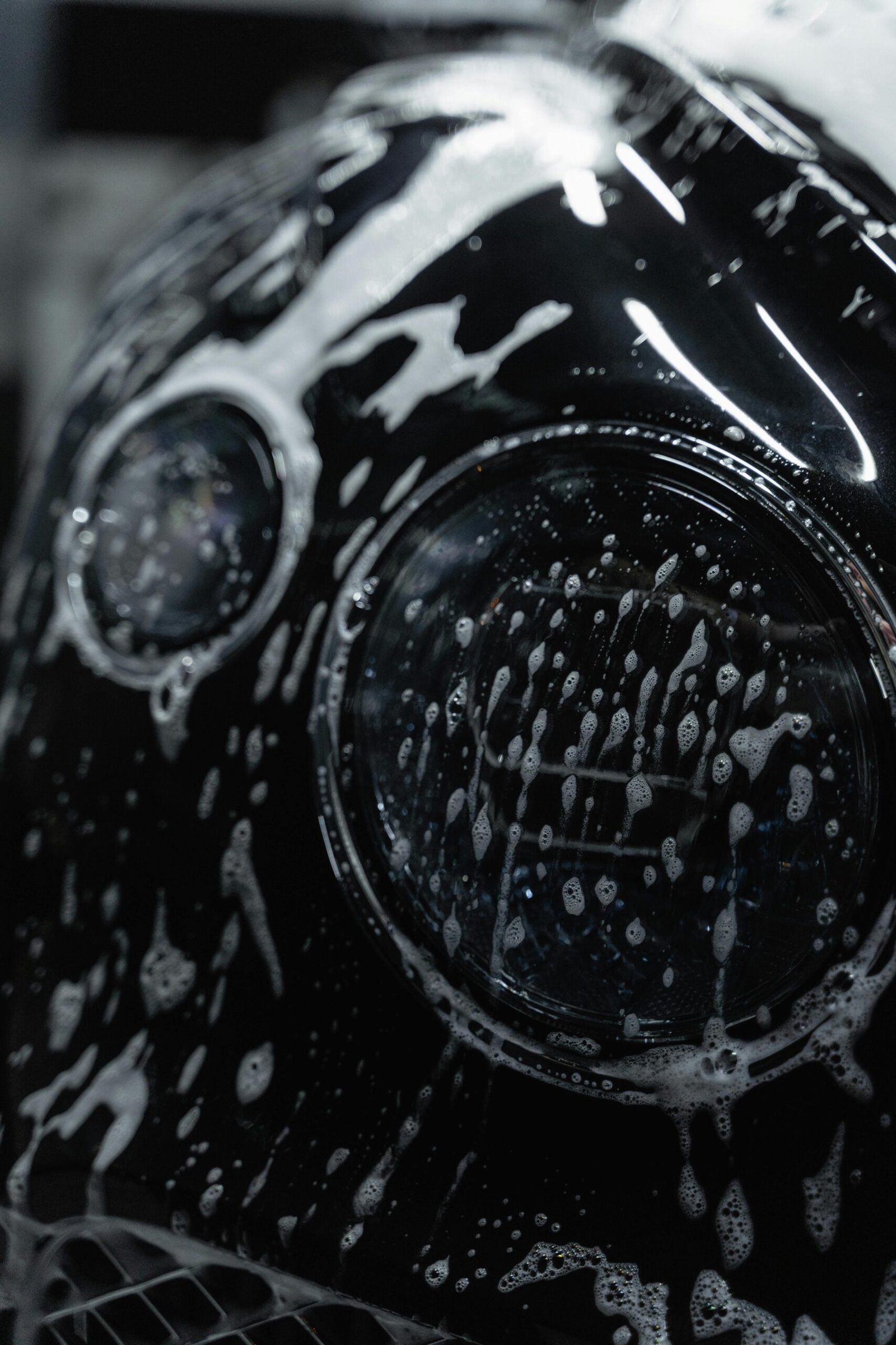 A detailed close-up of a car headlight covered with soap suds during a wash.