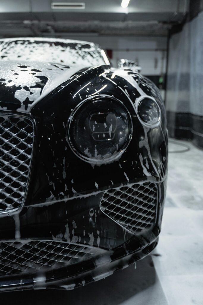 Close-up of a sleek black luxury car with soapy foam during a carwash process.