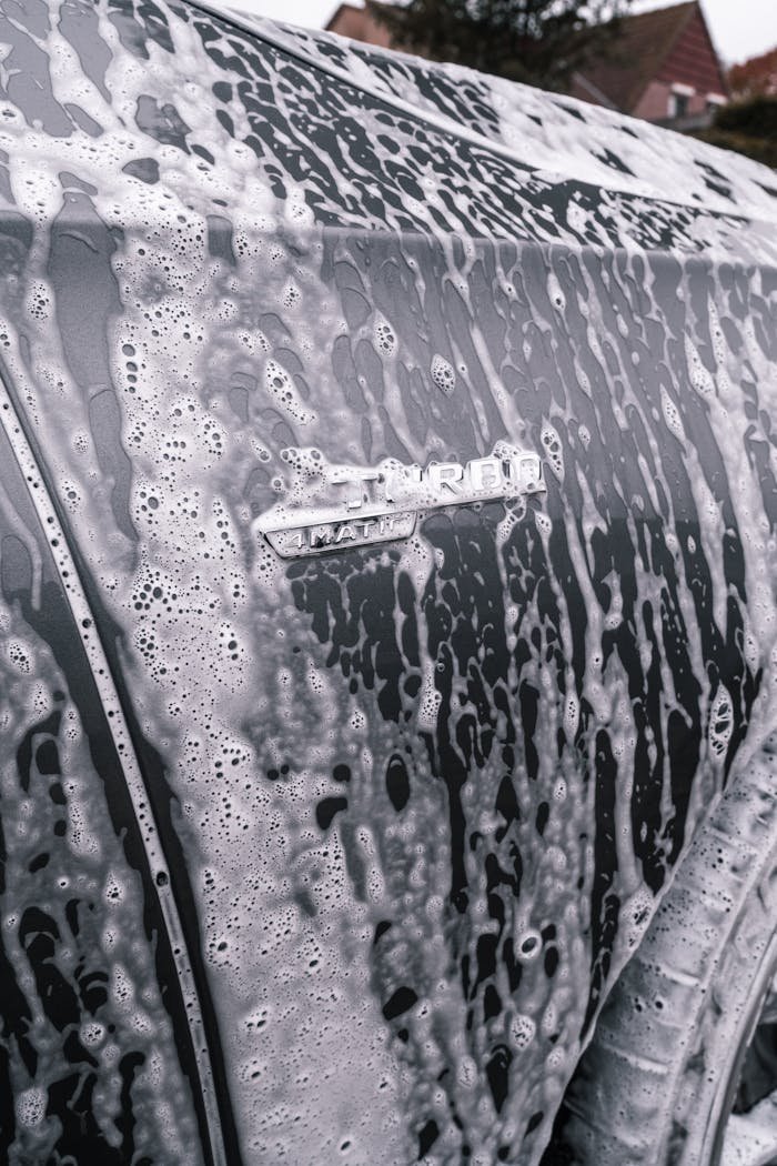 Detailed close-up shot of a car covered in soap suds during a wash, showcasing texture and cleaning process.
